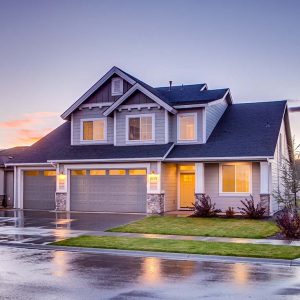 Two-story suburban home with asphalt roof seen from road on a rainy evening