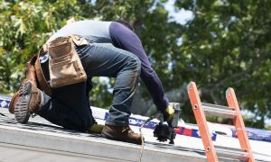 Contractor kneeling on a roof while completing roof repairs