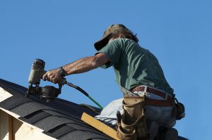 Roofer repairing an asphalt shingle roof under a blue sky