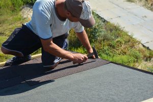 A roofing contractor is installing asphalt roofing shingles over underlayment on the edge of the roof